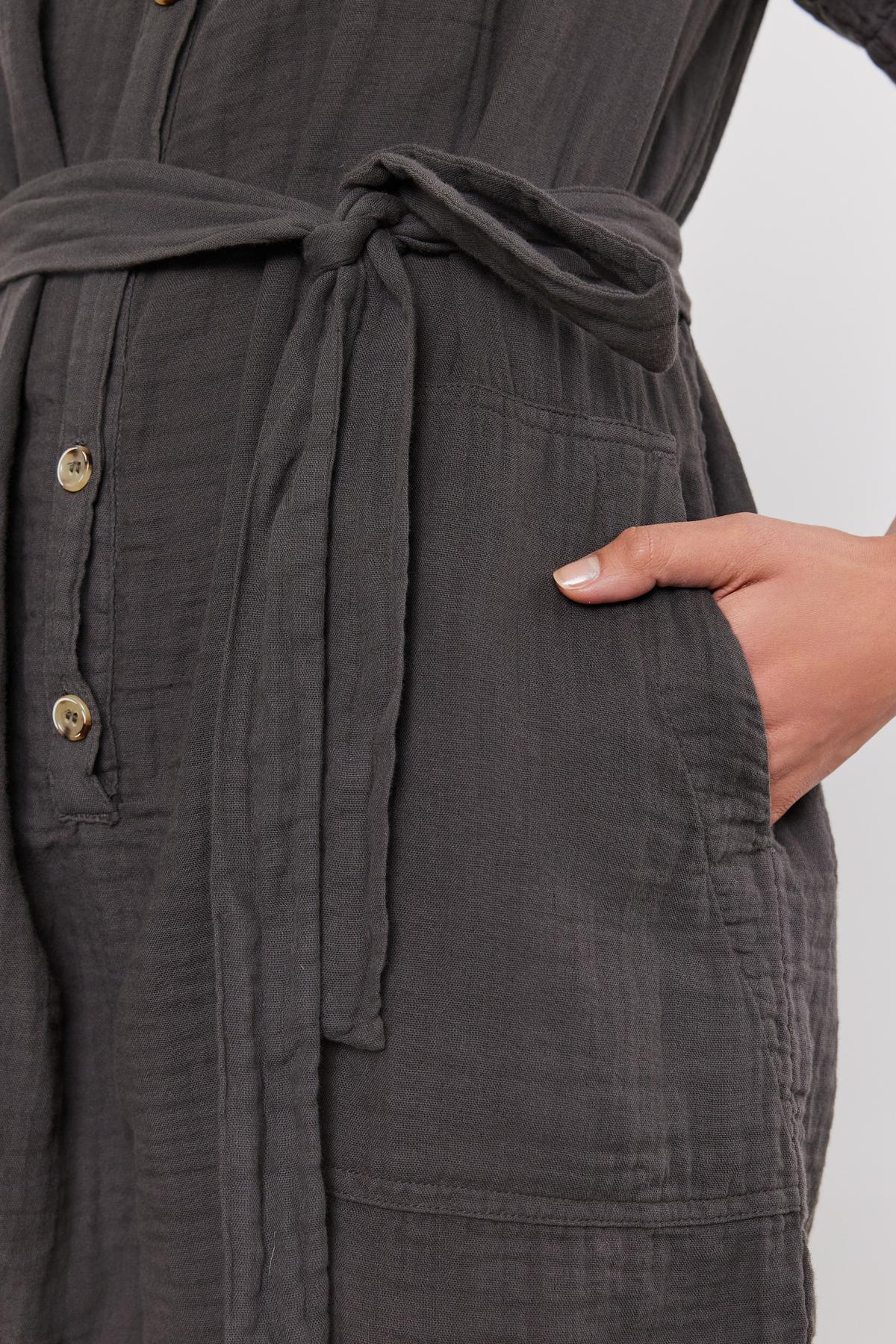   Close-up of a woman's hand resting on her hip, wearing a Velvet by Graham & Spencer DANE COTTON GAUZE ROMPER with a button front and tied waist. 