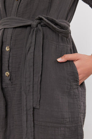 Close-up of a woman's hand resting on her hip, wearing a Velvet by Graham & Spencer DANE COTTON GAUZE ROMPER with a button front and tied waist.