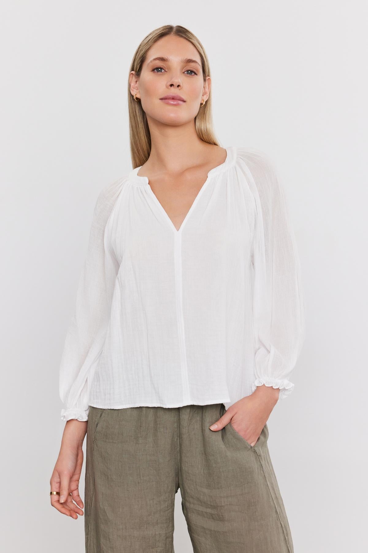 A woman in a Denice Cotton Gauze Top by Velvet by Graham & Spencer with sheer sleeves and green pants standing against a white background.-36910082457793