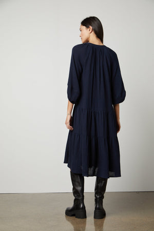 The back view of a woman wearing a Velvet by Graham & Spencer Dixon Cotton Gauze Tiered Dress and black boots.