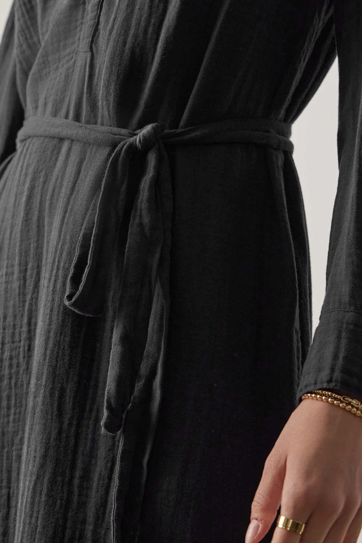   Close-up of a person wearing a black DOHENY DRESS by Velvet by Jenny Graham with shirred seams. Their right hand is visible, adorned with multiple rings and bracelets. 