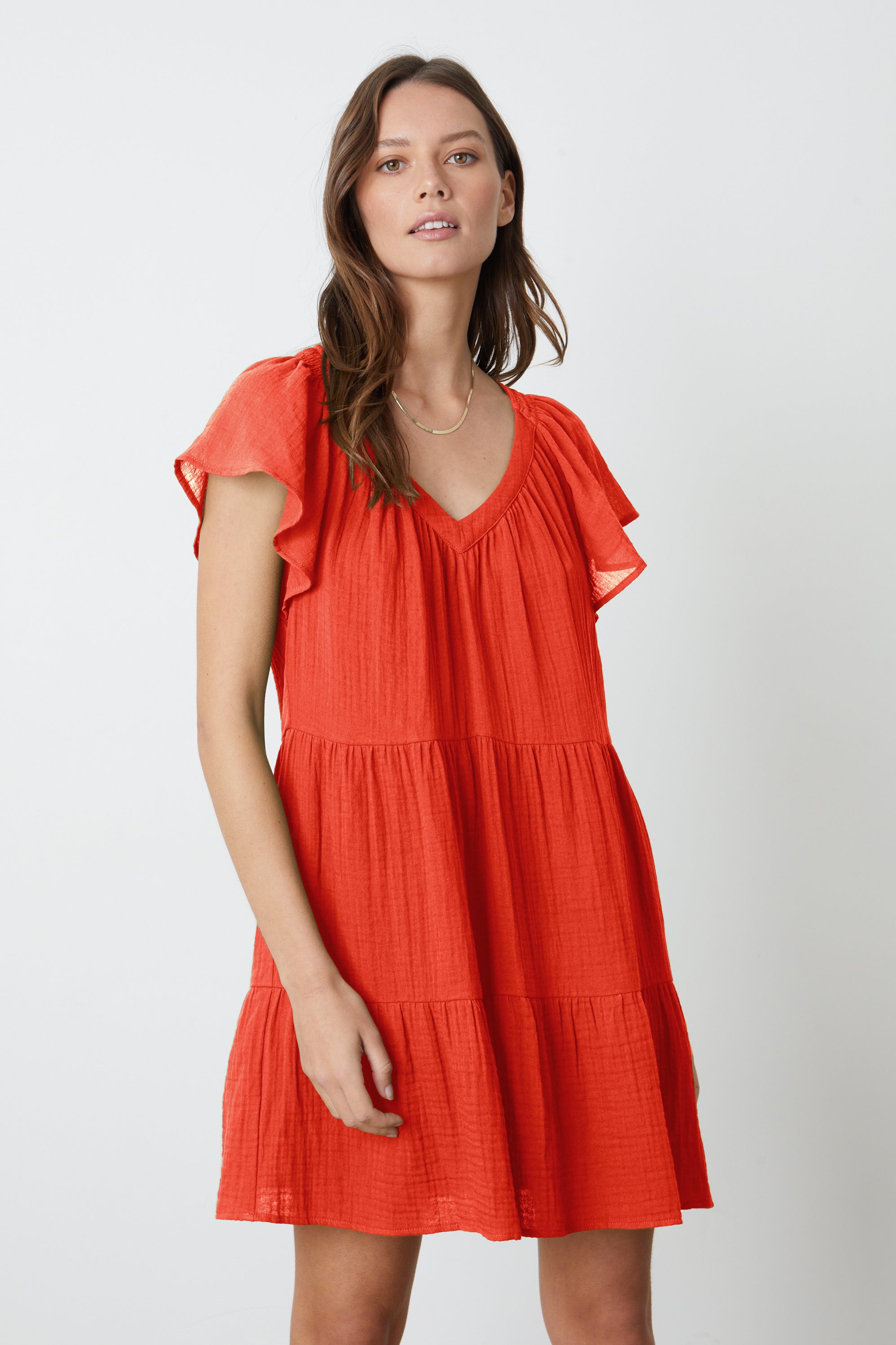   A woman wearing the ELEANOR COTTON GAUZE TIERED DRESS in cardinal red by Velvet by Graham & Spencer with ruffled sleeves. 