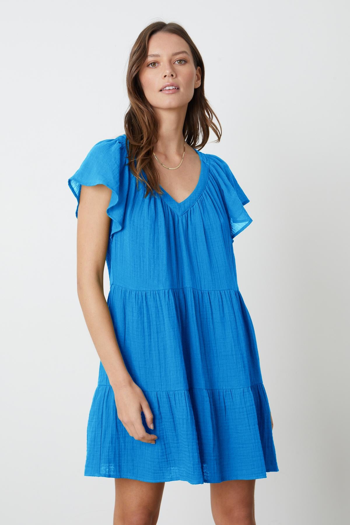 A woman is wearing the Velvet by Graham & Spencer ELEANOR COTTON GAUZE TIERED DRESS with frilled sleeves.-35201175355585