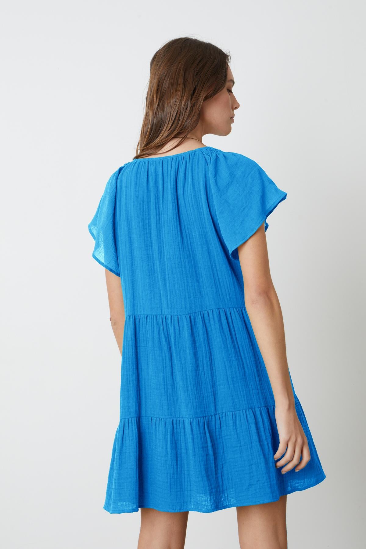 The back view of a woman wearing the Velvet by Graham & Spencer ELEANOR COTTON GAUZE TIERED DRESS with v-neckline and flutter sleeves.-35201175388353