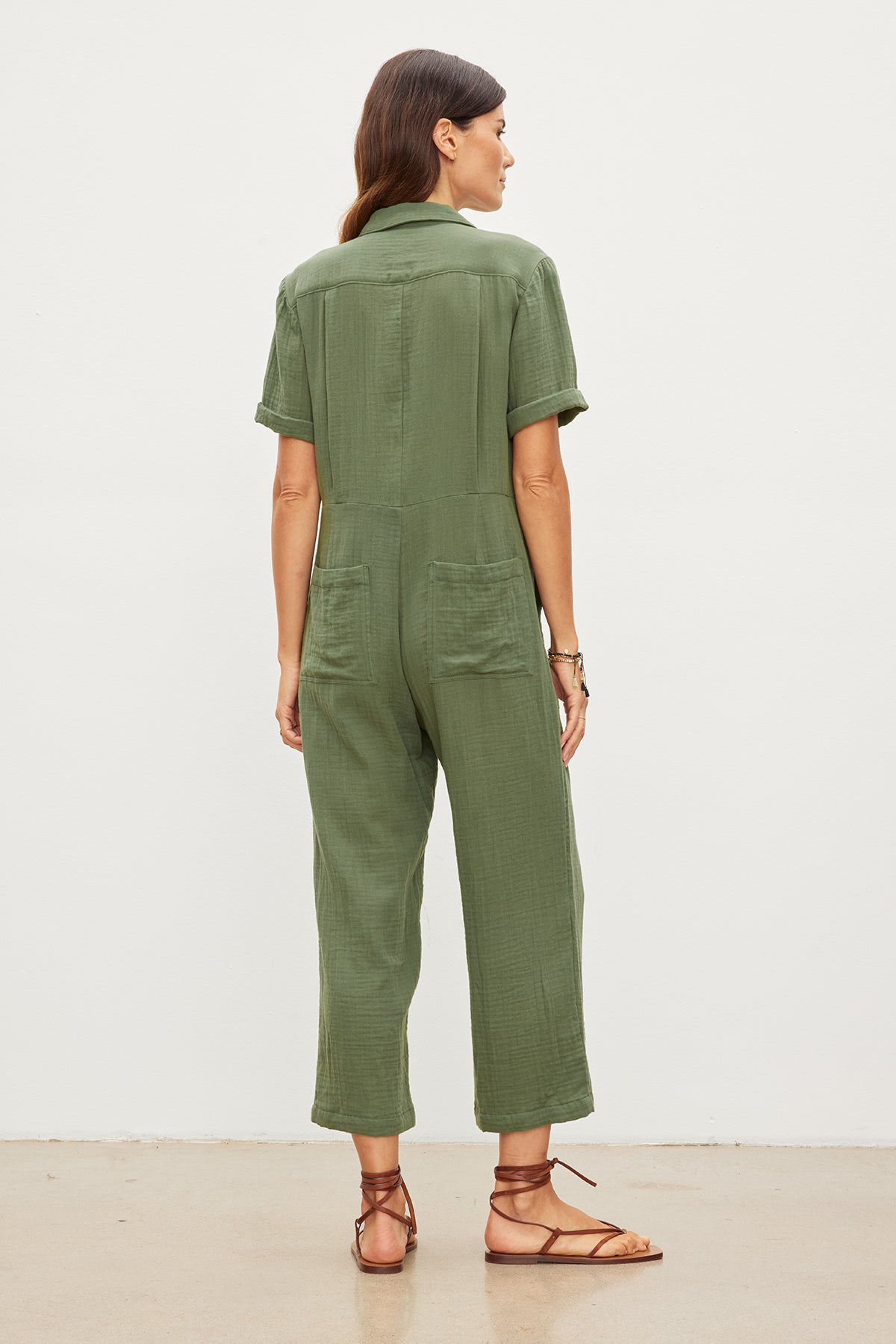   The back view of a relaxed woman wearing a green ELIA COTTON GAUZE JUMPSUIT with utilitarian detailing by Velvet by Graham & Spencer. 