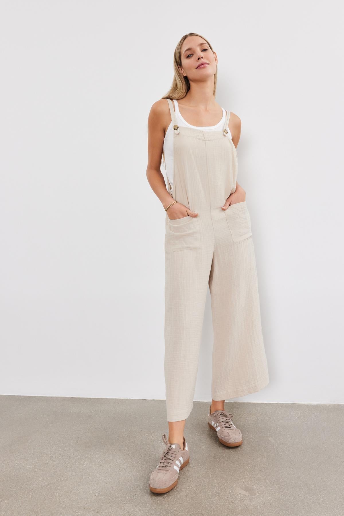  A young woman stands confidently, wearing a Velvet by Graham & Spencer EVERLEE COTTON GAUZE JUMPSUIT with sneakers, against a plain white backdrop. 