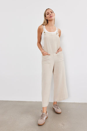 A young woman stands confidently, wearing a Velvet by Graham & Spencer EVERLEE COTTON GAUZE JUMPSUIT with sneakers, against a plain white backdrop.
