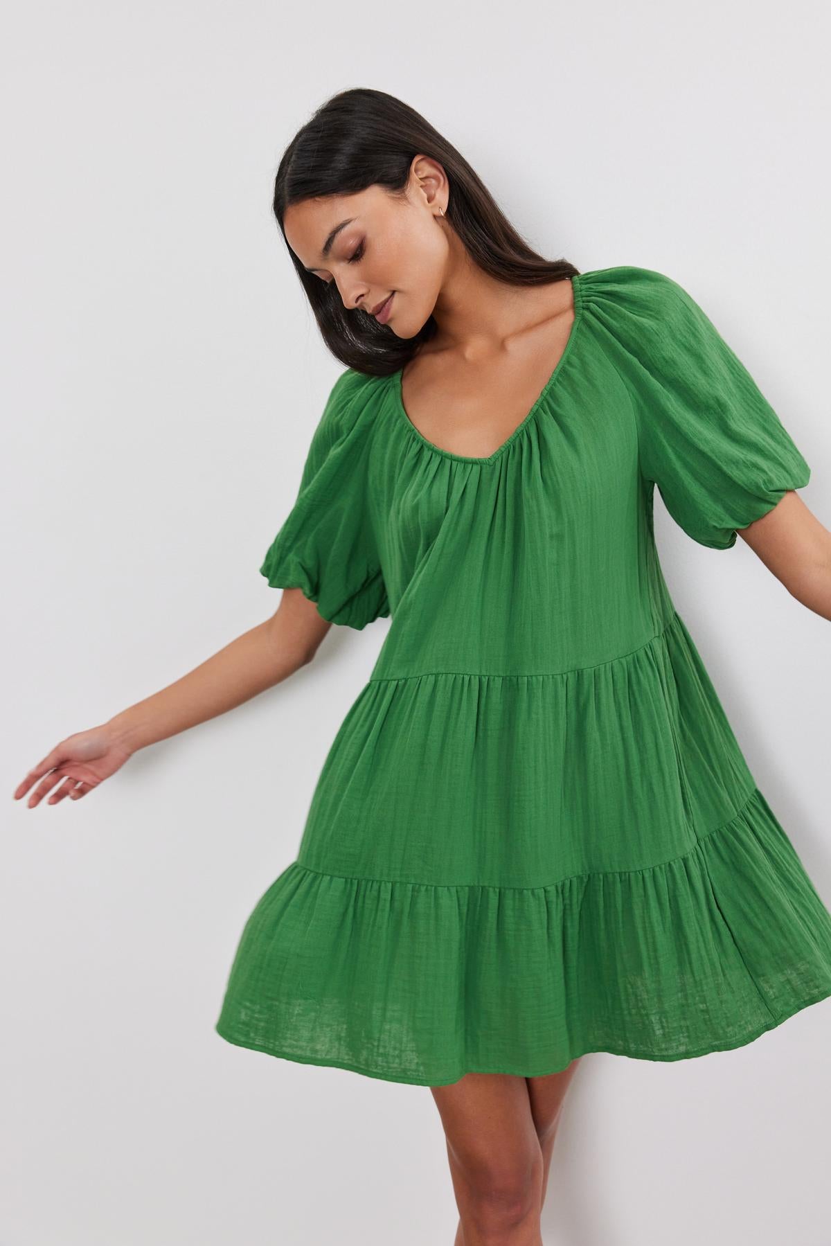   Woman in a green Helena Cotton Gauze Dress by Velvet by Graham & Spencer with puff sleeves and a two-tiered silhouette, standing against a white background. 