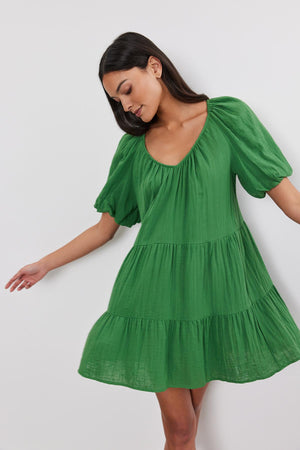 Woman in a green Helena Cotton Gauze Dress by Velvet by Graham & Spencer with puff sleeves and a two-tiered silhouette, standing against a white background.