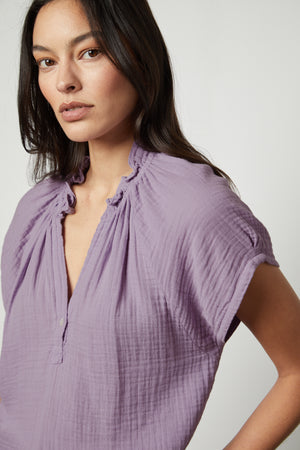 The model is wearing a purple JADEN COTTON GAUZE V-NECK TOP with ruffles by Velvet by Graham & Spencer.