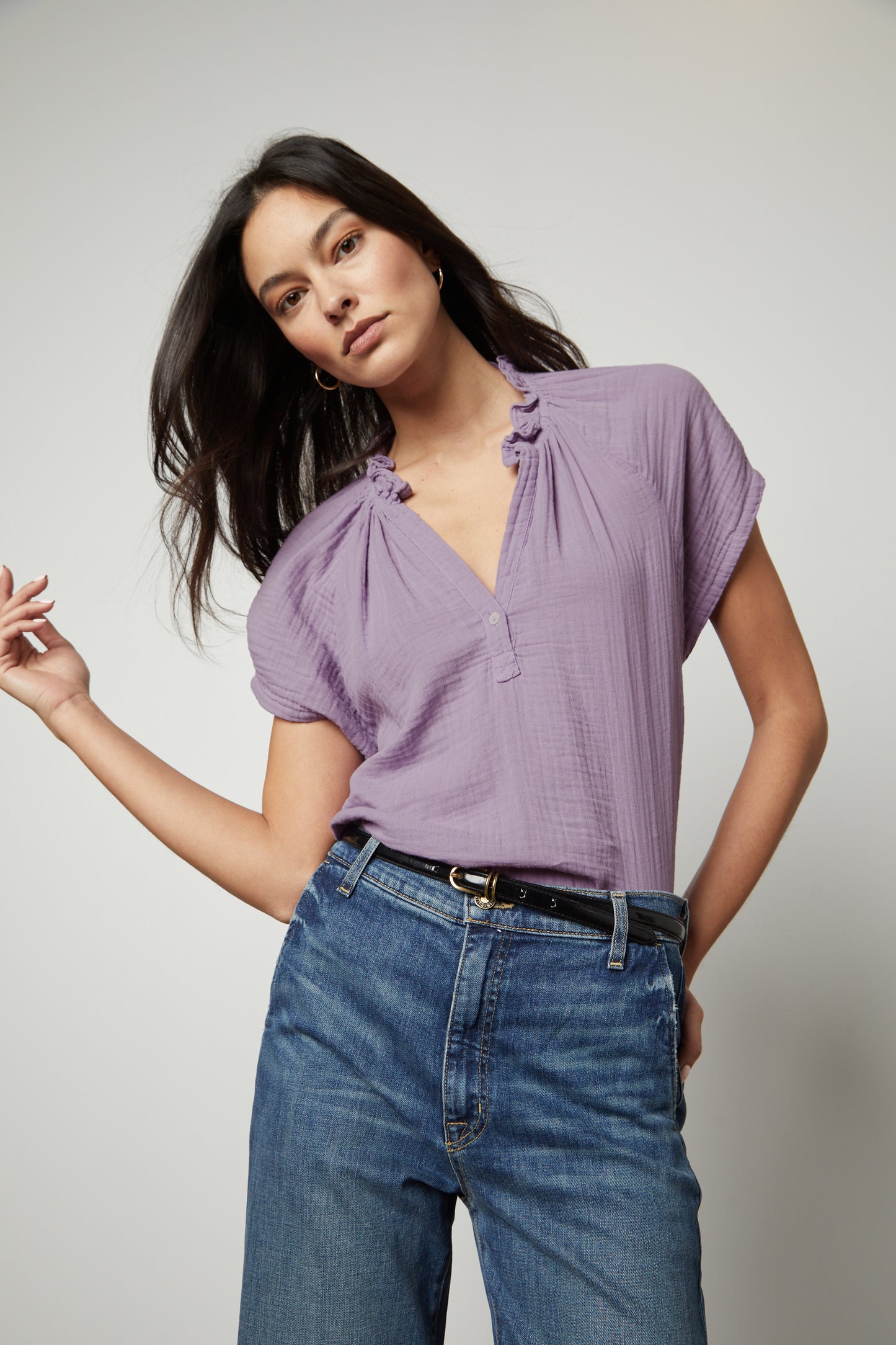 The model is wearing a JADEN COTTON GAUZE V-NECK TOP by Velvet by Graham & Spencer in a purple color and pairing it with blue jeans.-35656762196161