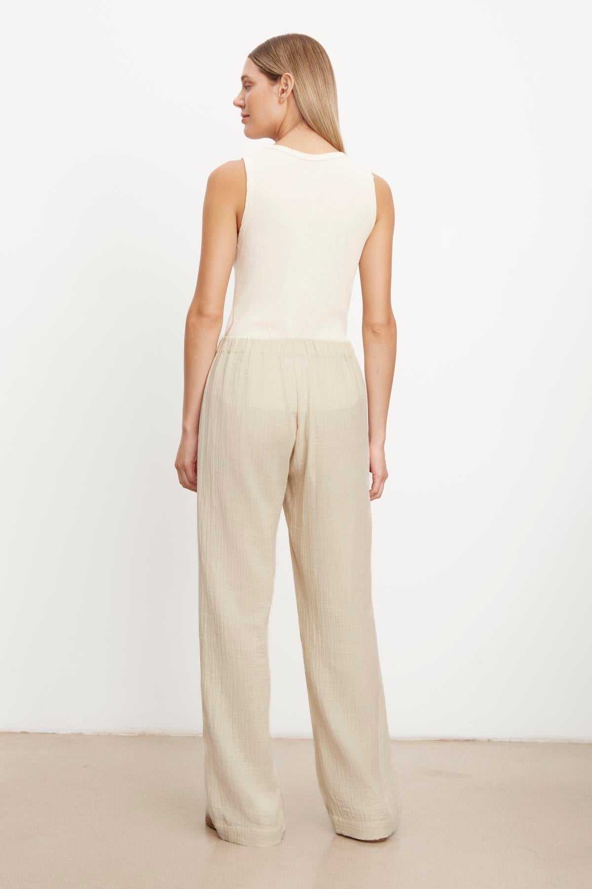   Woman standing in a neutral position wearing a sleeveless top and beige, lightweight Velvet by Graham & Spencer JERRY COTTON GAUZE PANT trousers with an elastic waistband against a plain background. 