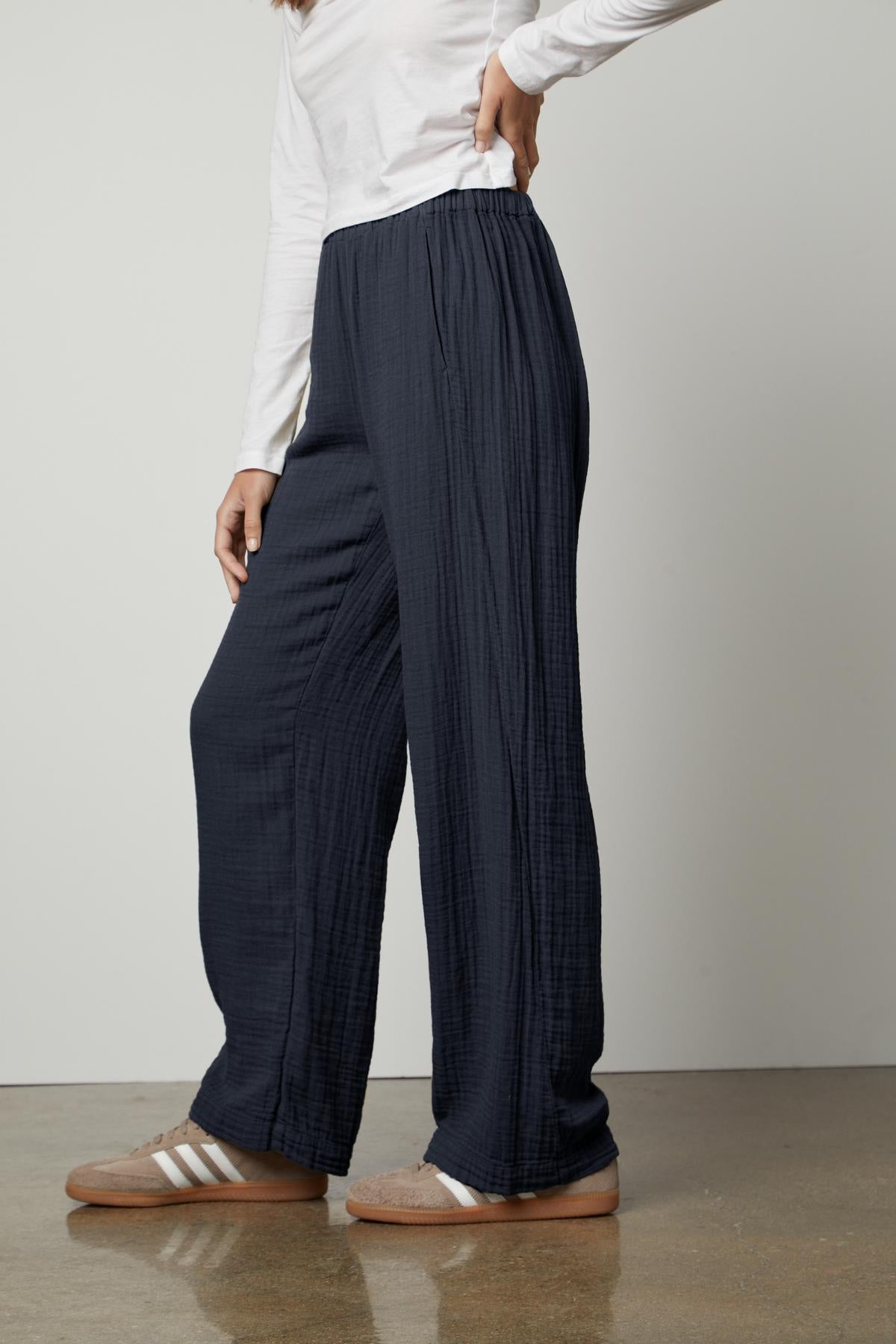   Woman wearing Velvet by Graham & Spencer navy blue straight leg pants and white top, paired with brown slide sandals. 