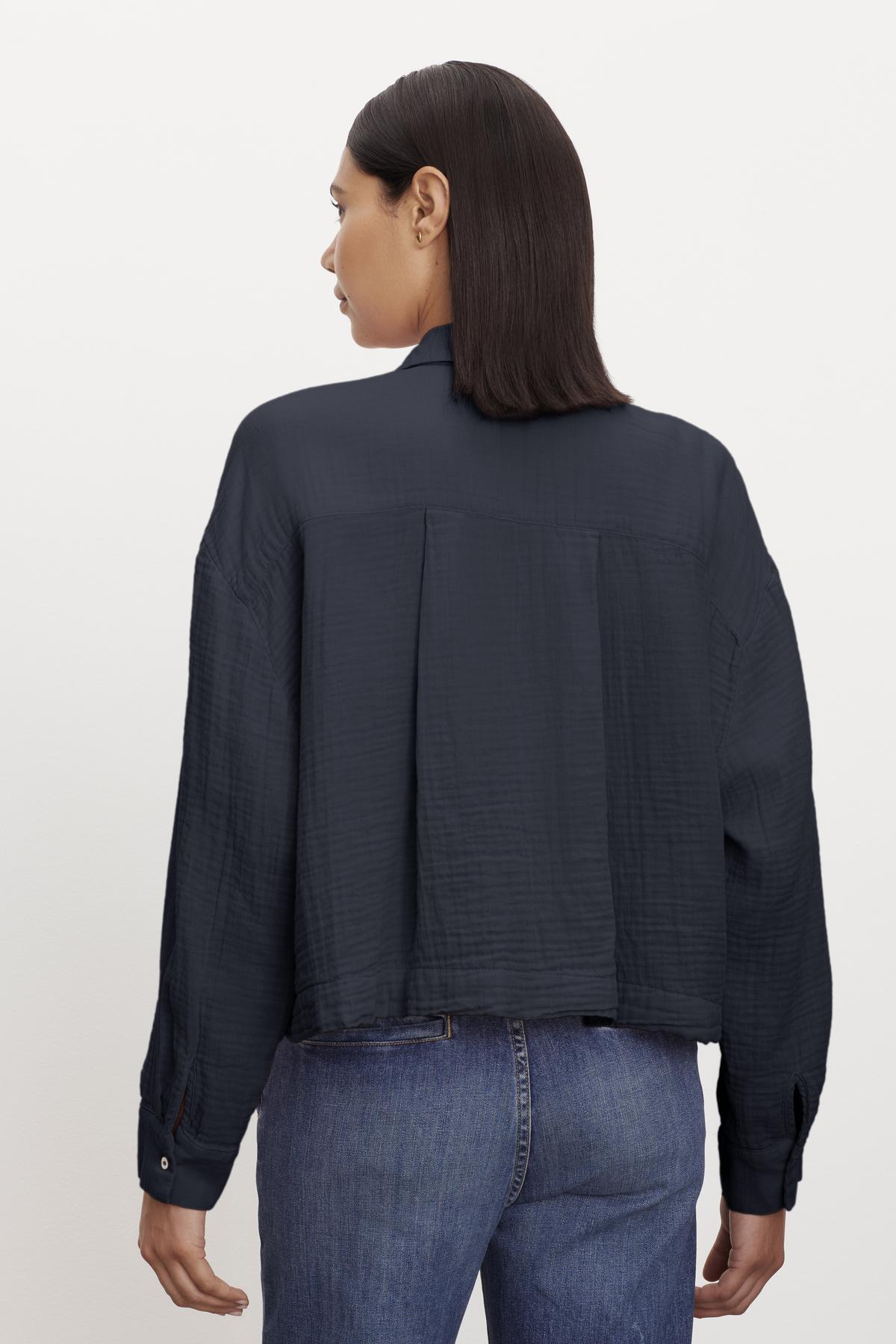 Woman in a cropped LANA COTTON GAUZE BUTTON-UP SHIRT blouse by Velvet by Graham & Spencer and blue jeans viewed from behind.-36462890287297