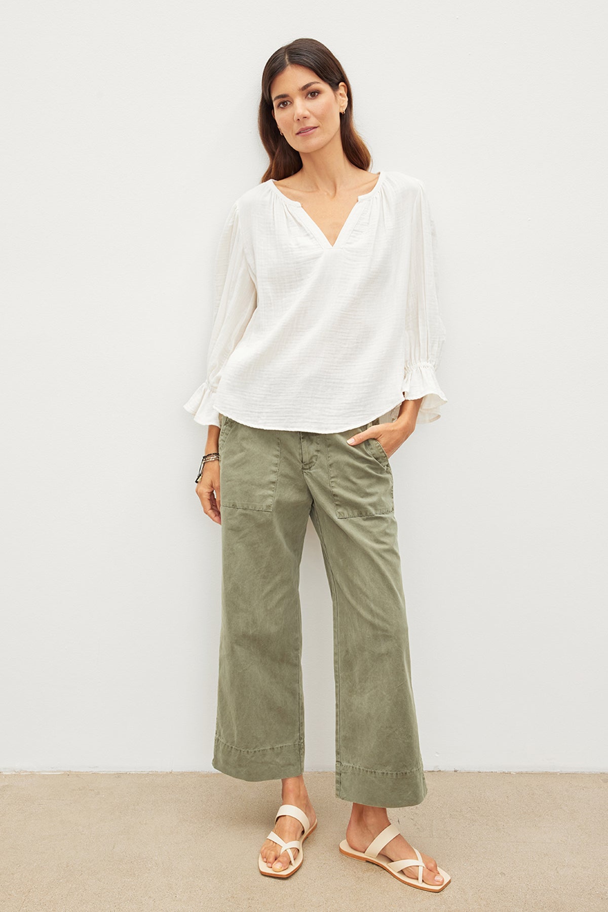 A woman in a white blouse and green pants exudes effortless sophistication with her Velvet by Graham & Spencer MILLY COTTON GAUZE PEASANT TOP outfit.-35967572934849