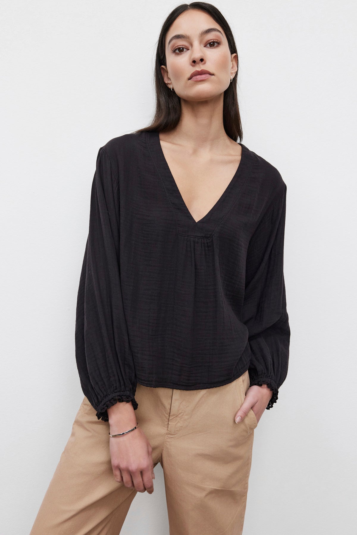   A person wearing a black Naomi Cotton Gauze Top by Velvet by Graham & Spencer with a relaxed fit, paired with light brown pants, stands against a plain white background. 