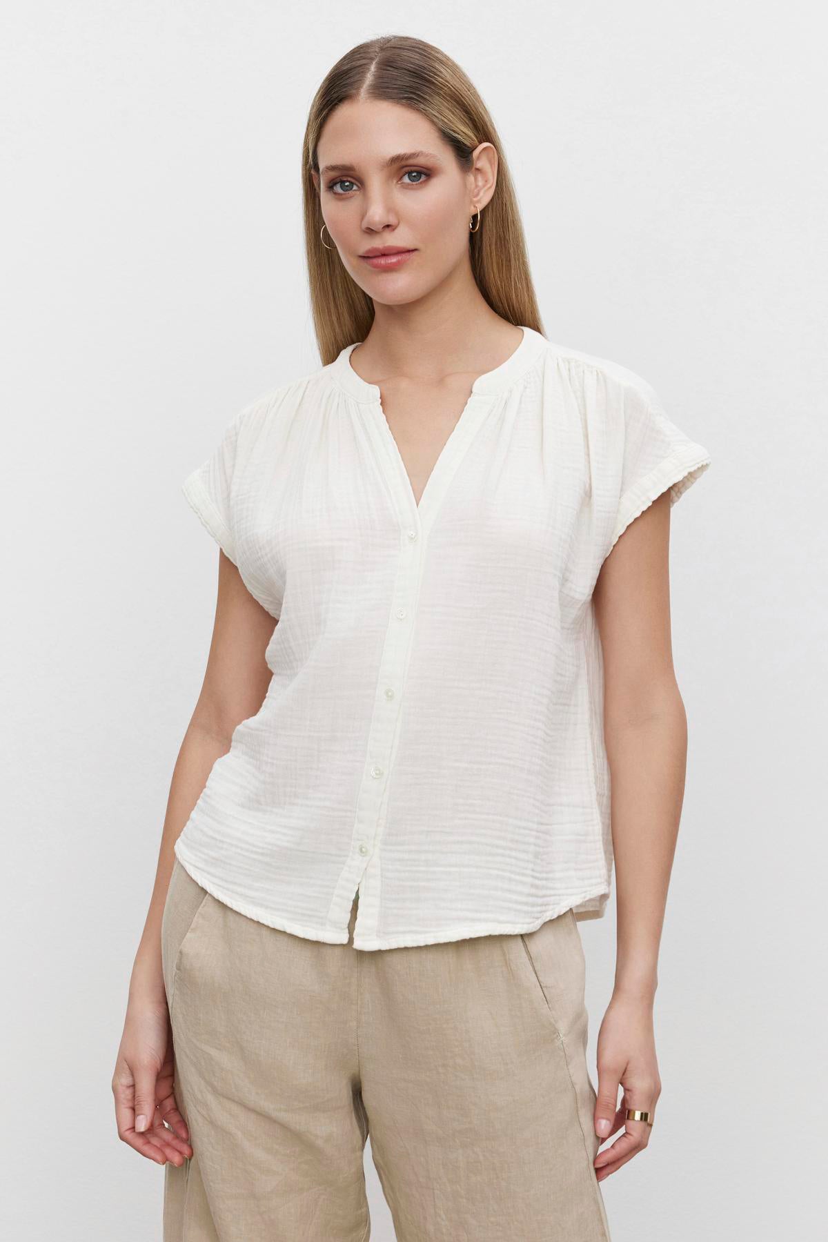   Woman in a Velvet by Graham & Spencer PAMELA COTTON GAUZE BUTTON-UP TOP white blouse and beige trousers standing against a plain background. 