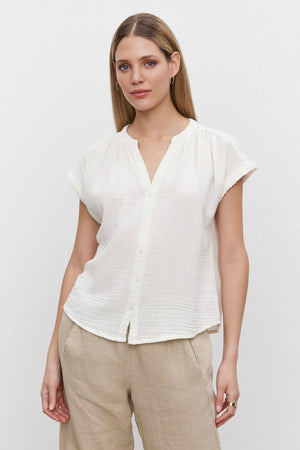 Woman in a Velvet by Graham & Spencer PAMELA COTTON GAUZE BUTTON-UP TOP white blouse and beige trousers standing against a plain background.