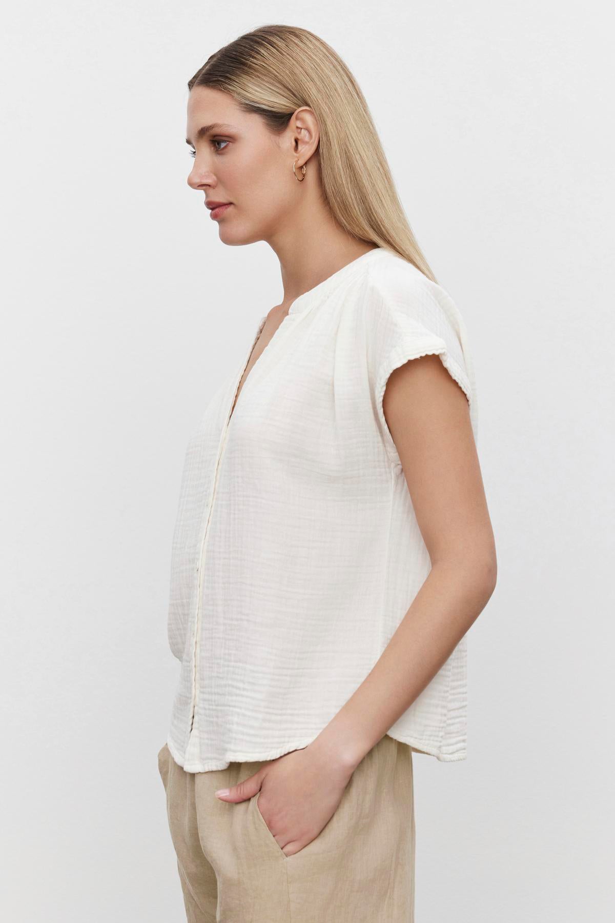   Profile view of a woman wearing a Pamela Cotton Gauze Button-Up Top by Velvet by Graham & Spencer and beige pants, embodying a relaxed silhouette perfect for spring weekend fashion. 