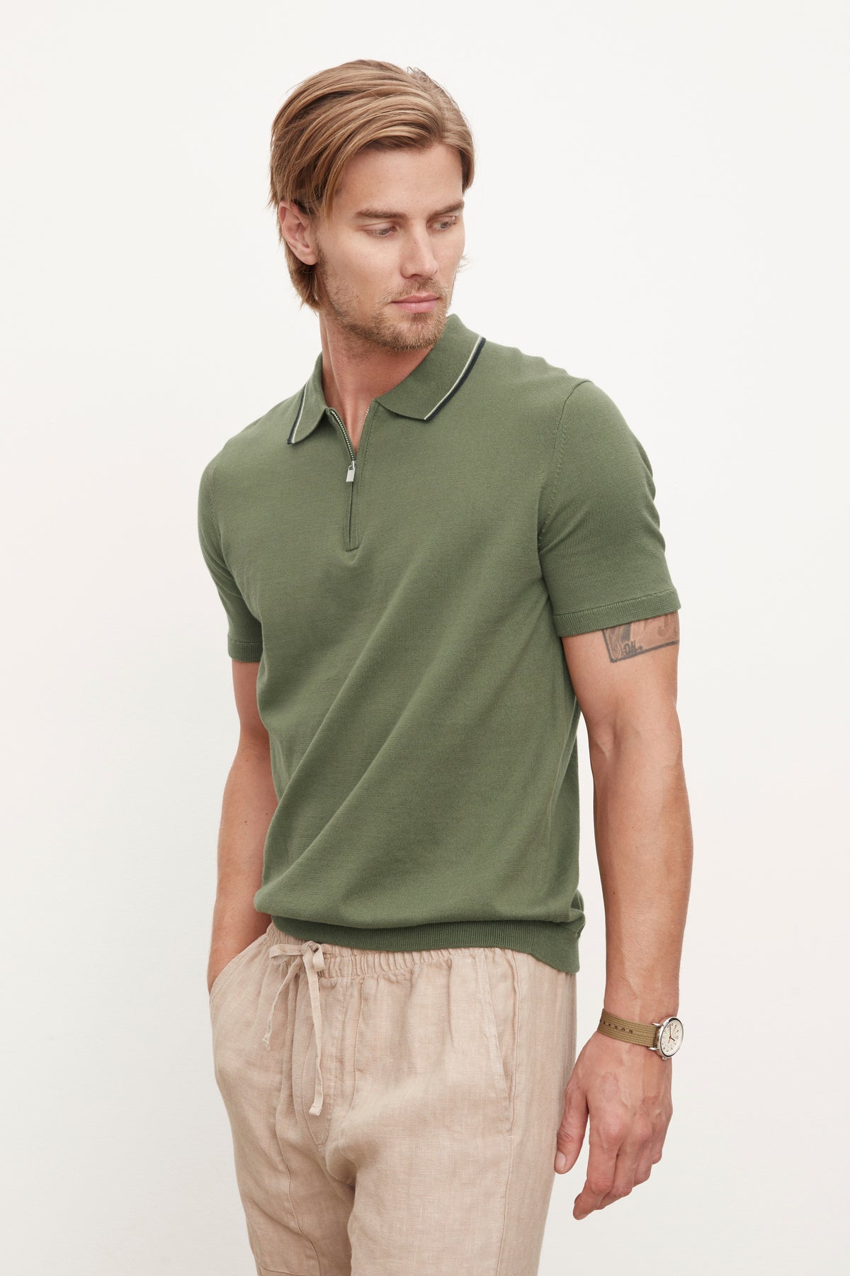   The model is wearing a green OTTO ZIP POLO shirt and tan pants. 
