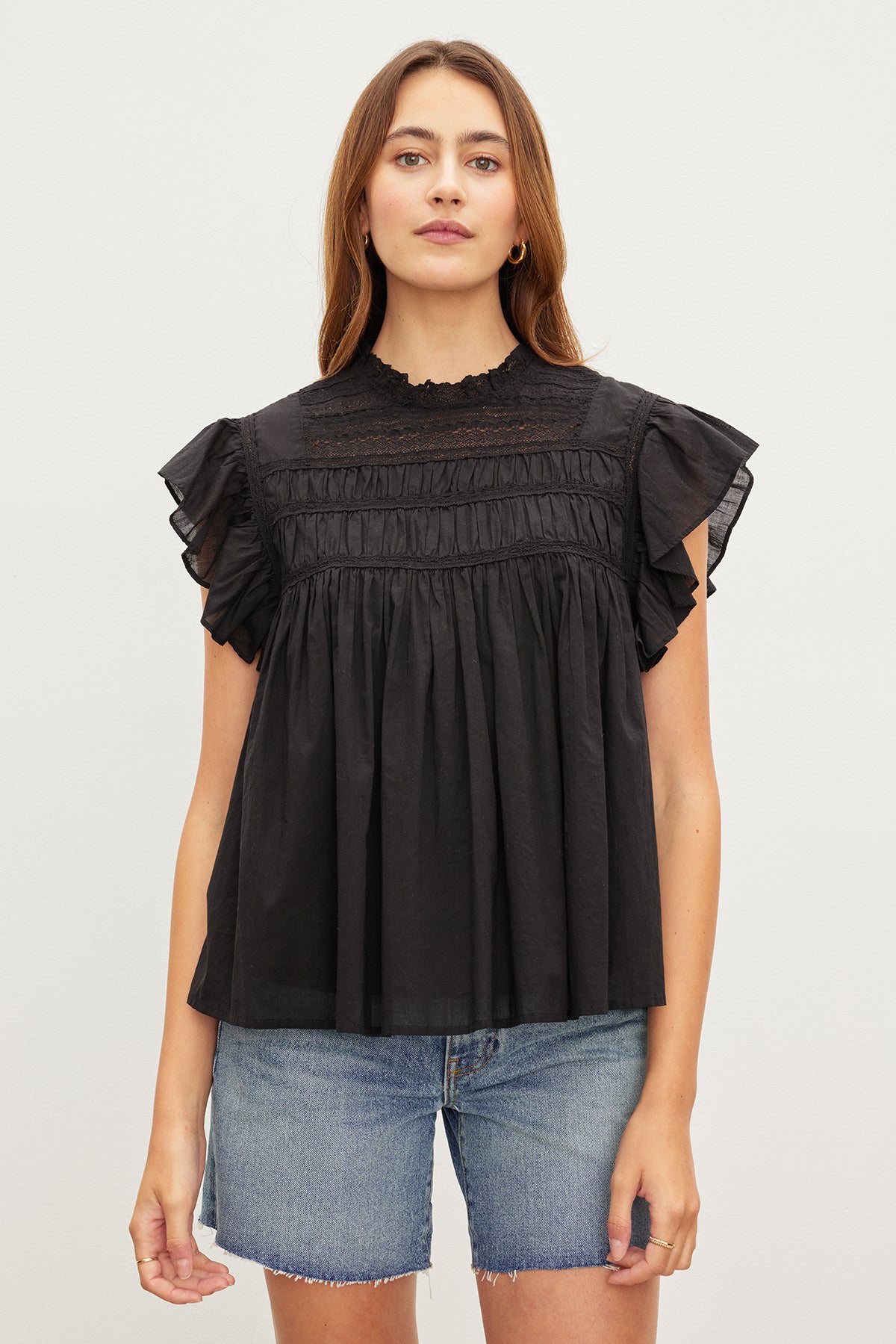  A woman wearing the INESSA COTTON LACE TOP by Velvet by Graham & Spencer, a black top with ruffled sleeves. 