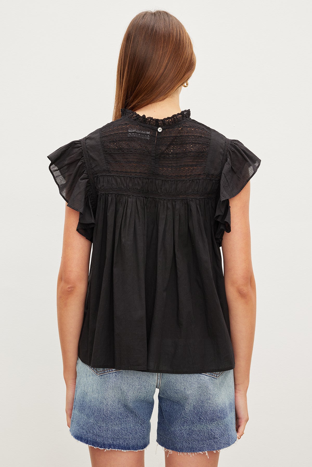 The back view of a woman wearing an INESSA COTTON LACE TOP by Velvet by Graham & Spencer with ruffled sleeves.-35967734317249