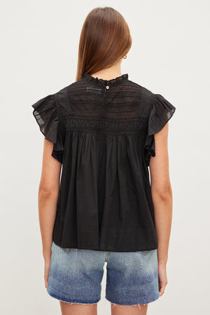 The back view of a woman wearing an INESSA COTTON LACE TOP by Velvet by Graham & Spencer with ruffled sleeves.