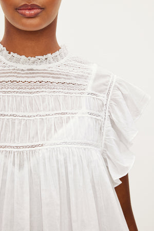 A woman is wearing a INESSA COTTON LACE TOP by Velvet by Graham & Spencer, with ruffles.