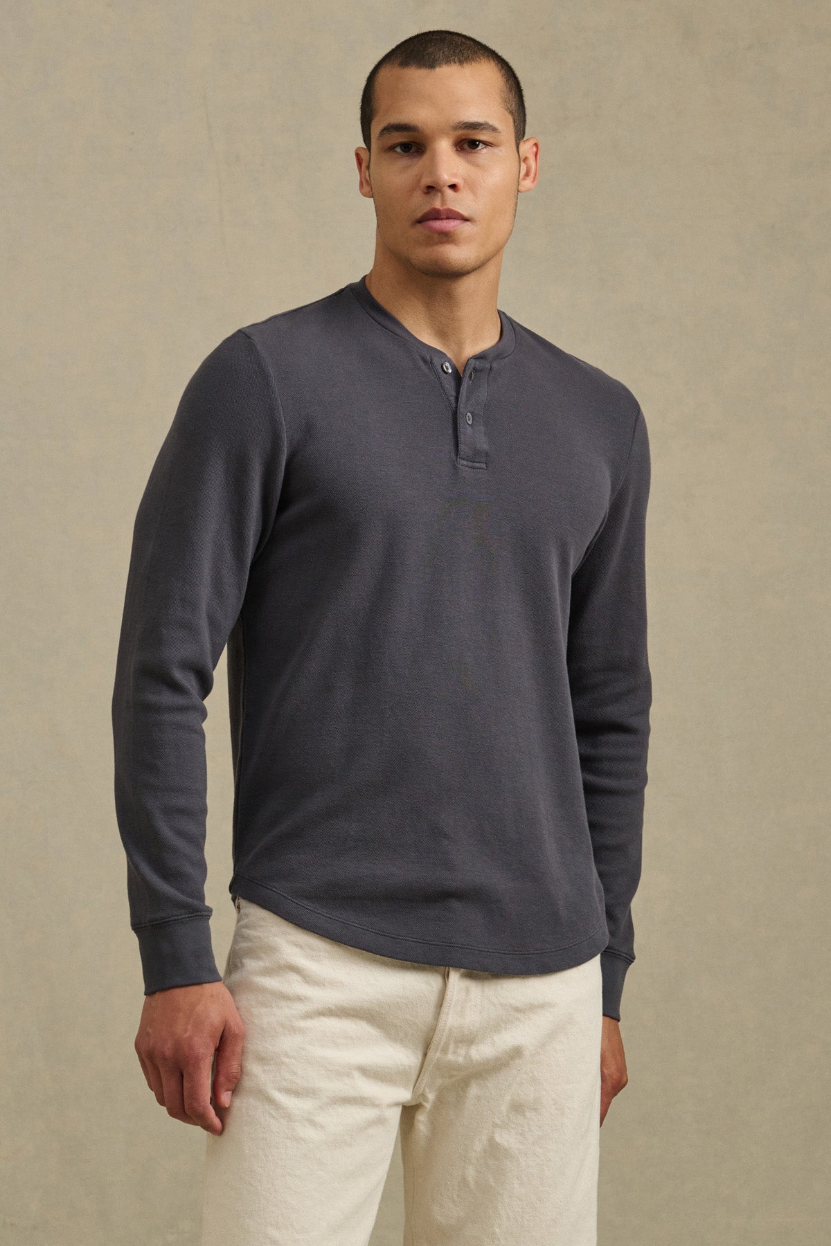 A man stands facing forward, wearing the ARNOLD HENLEY by Velvet by Graham & Spencer in dark gray and off-white pants against a plain beige background.-41374344347841