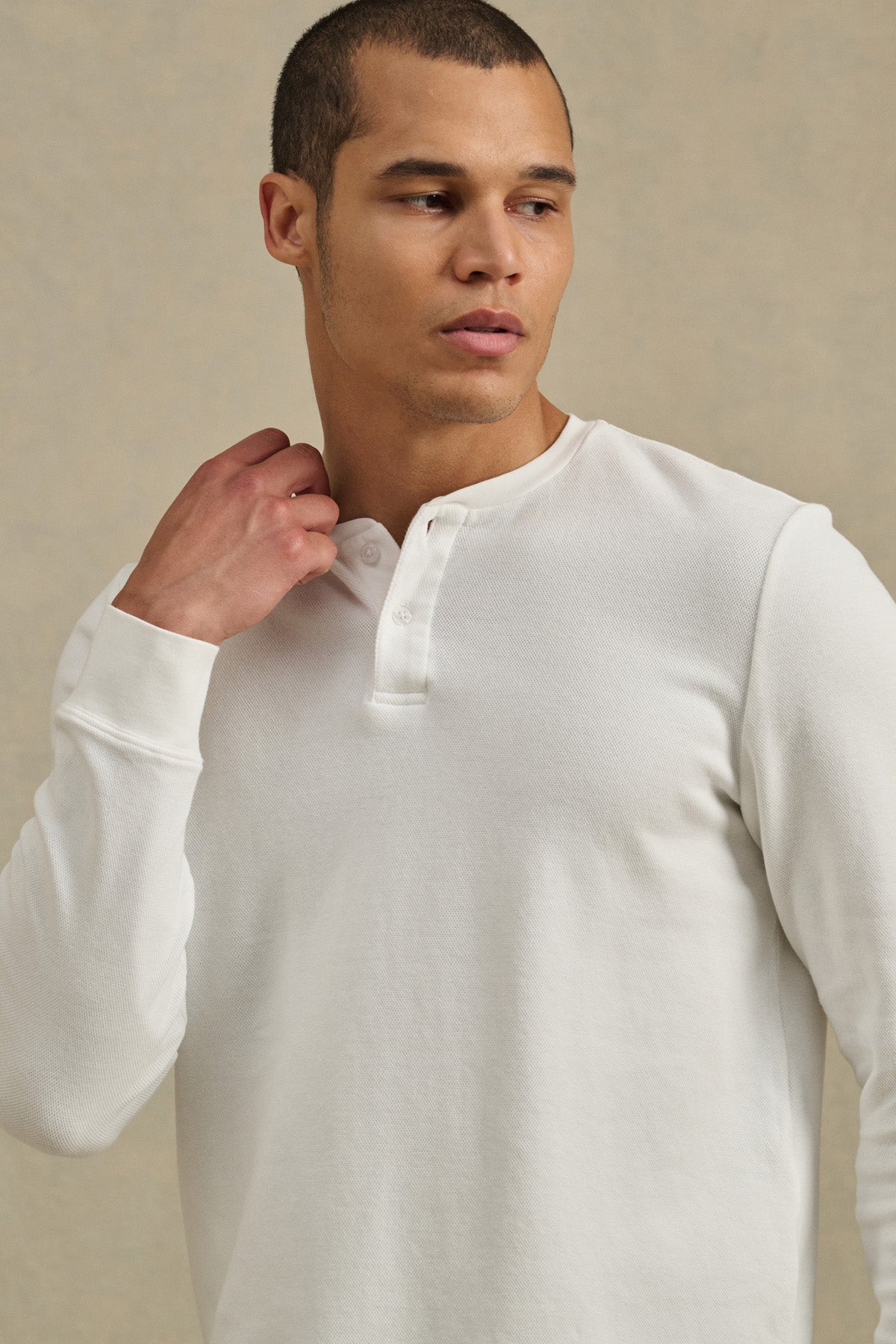 A man wearing the ARNOLD HENLEY by Velvet by Graham & Spencer looks to his left, touching the collar with one hand.-41374344708289