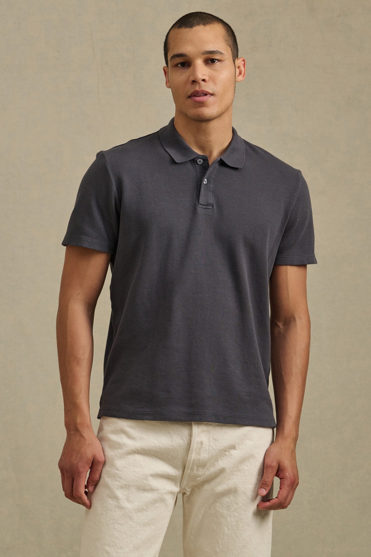 A man wearing the JOHNNY POLO by Velvet by Graham & Spencer in dark gray with off-white pants stands against a plain neutral background.-41374394056897