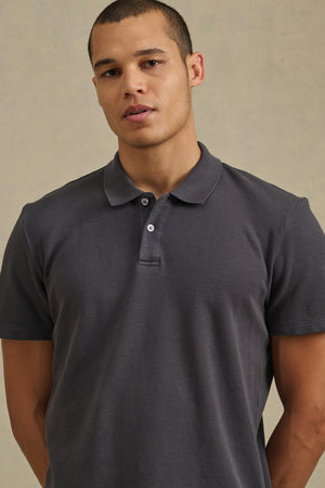 A man models the Velvet by Graham & Spencer JOHNNY POLO, a short-sleeve dark gray shirt, against a plain light background.