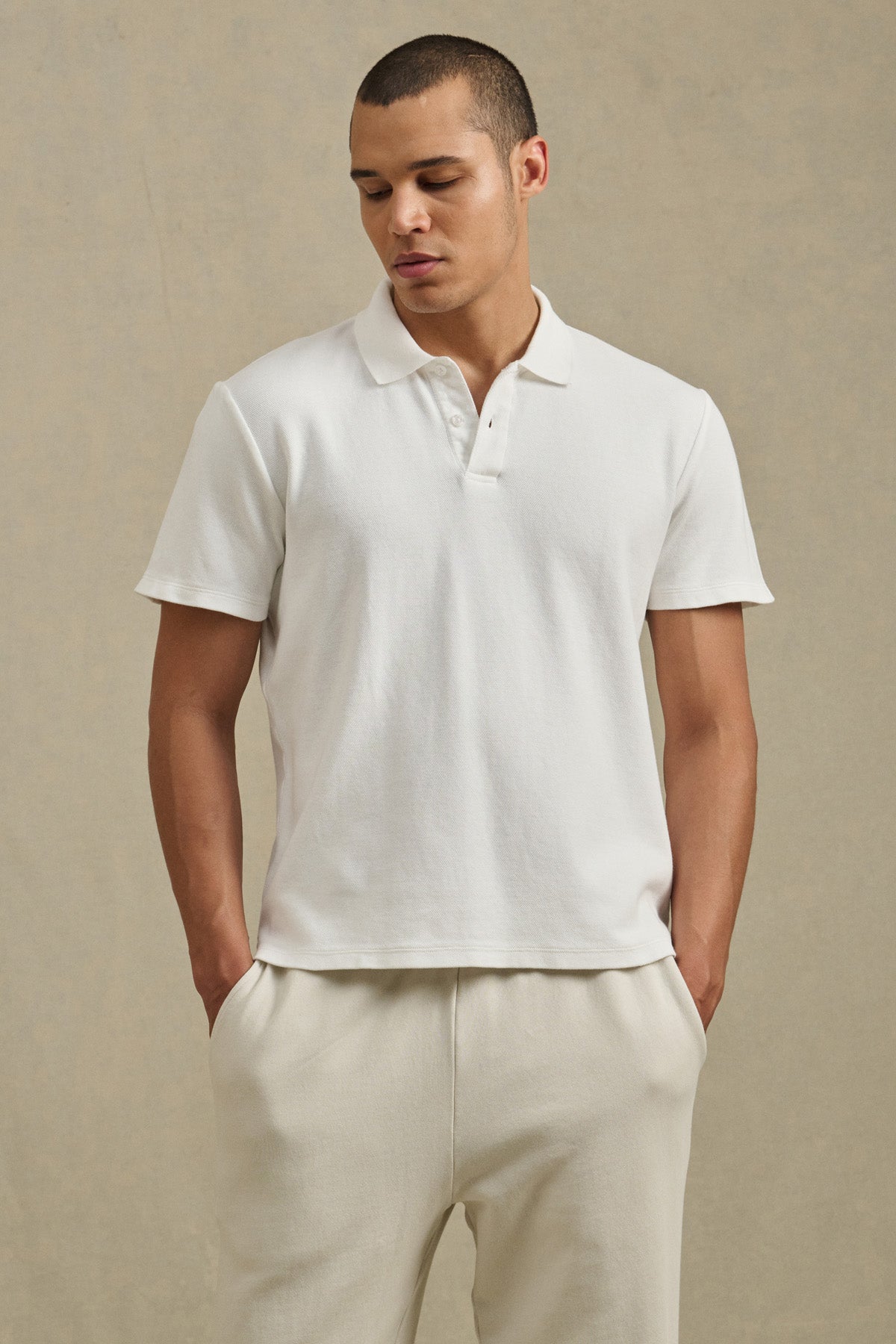 A man stands with his hands in his pockets against a neutral background, wearing the JOHNNY POLO by Velvet by Graham & Spencer and light-colored pants.-41428156416193