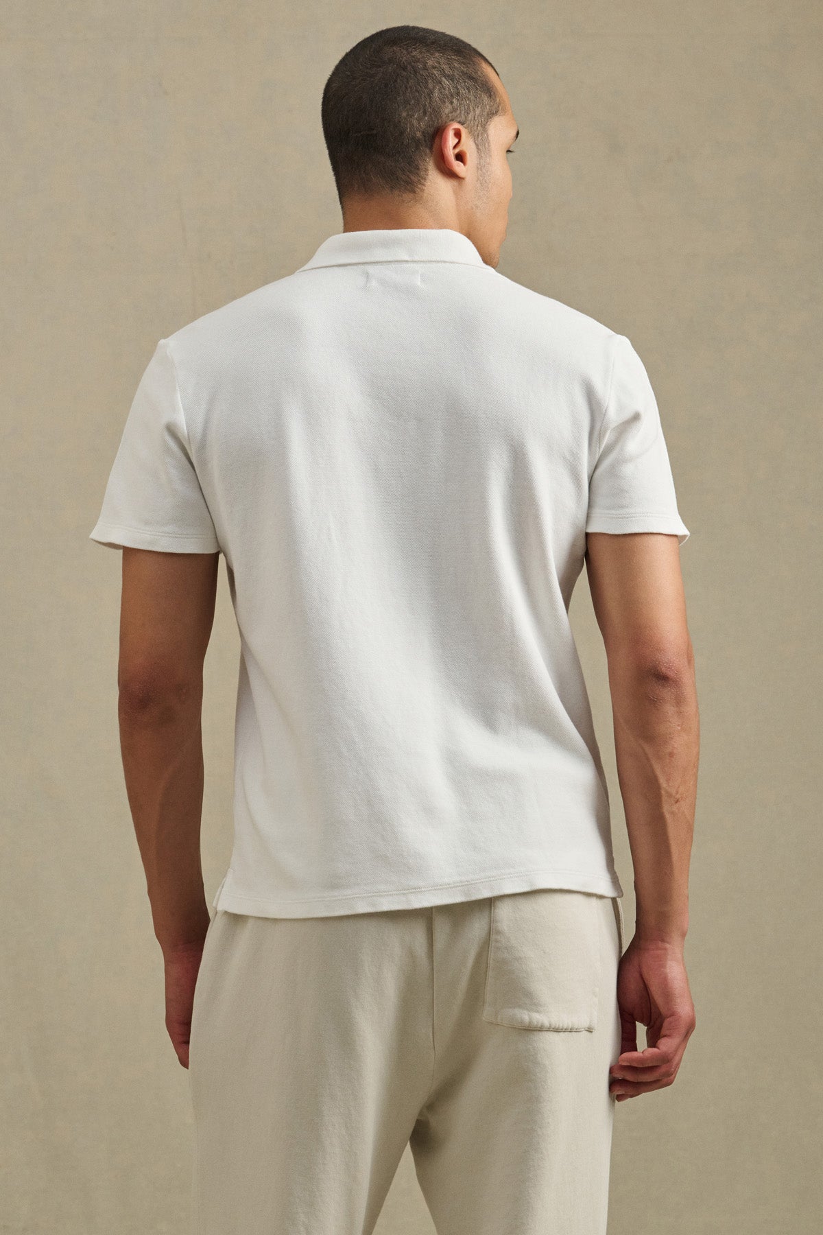 A man faces away from the camera in the Velvet by Graham & Spencer JOHNNY POLO, a breathable cotton mesh shirt, paired with light pants against a neutral background.
