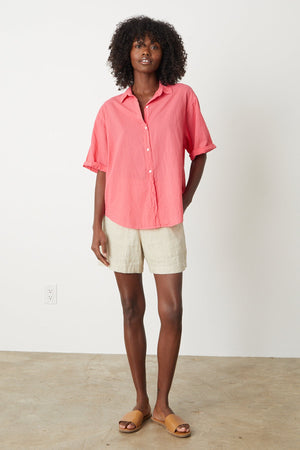 The model is wearing a Velvet by Graham & Spencer SHANNON BUTTON-UP SHIRT in pink and tan shorts.