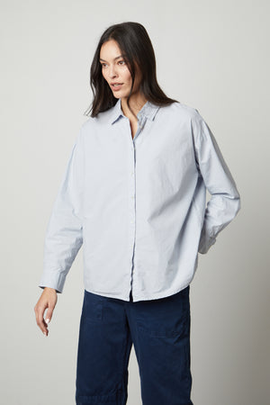 The model is wearing a DAKOTA BUTTON-UP SHIRT by Velvet by Graham & Spencer and blue pants with a classic modern design.