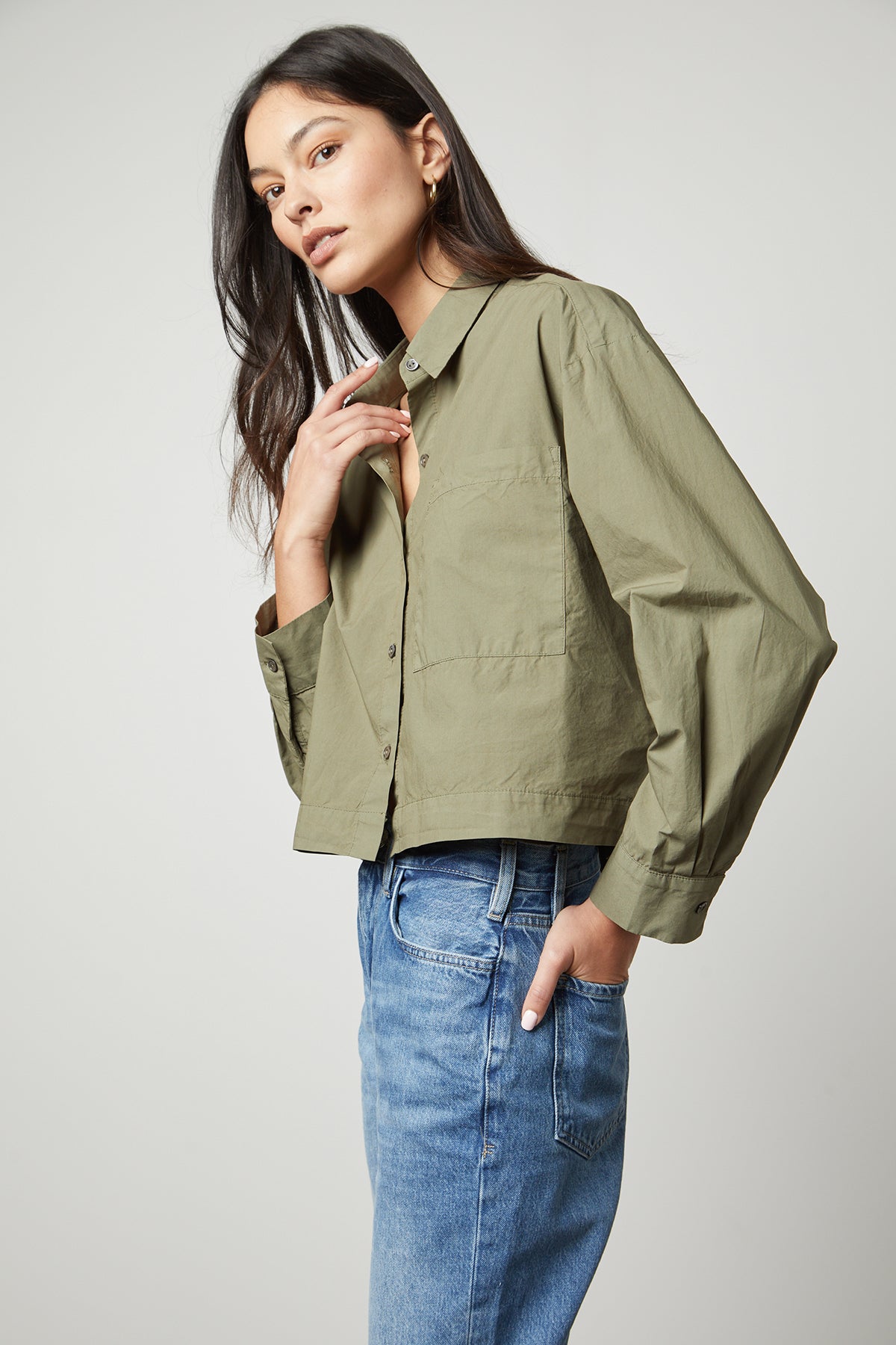 The model is wearing a LUCILLE CROPPED BUTTON-UP SHIRT by Velvet by Graham & Spencer with an oversized single pocket and jeans.-35503727804609