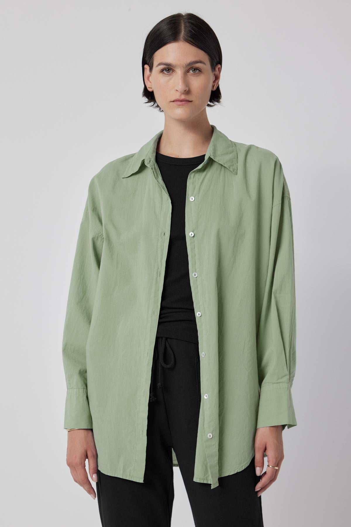 A woman wearing an oversized green REDONDO BUTTON-UP SHIRT by Velvet by Jenny Graham and black pants.-36198179995841