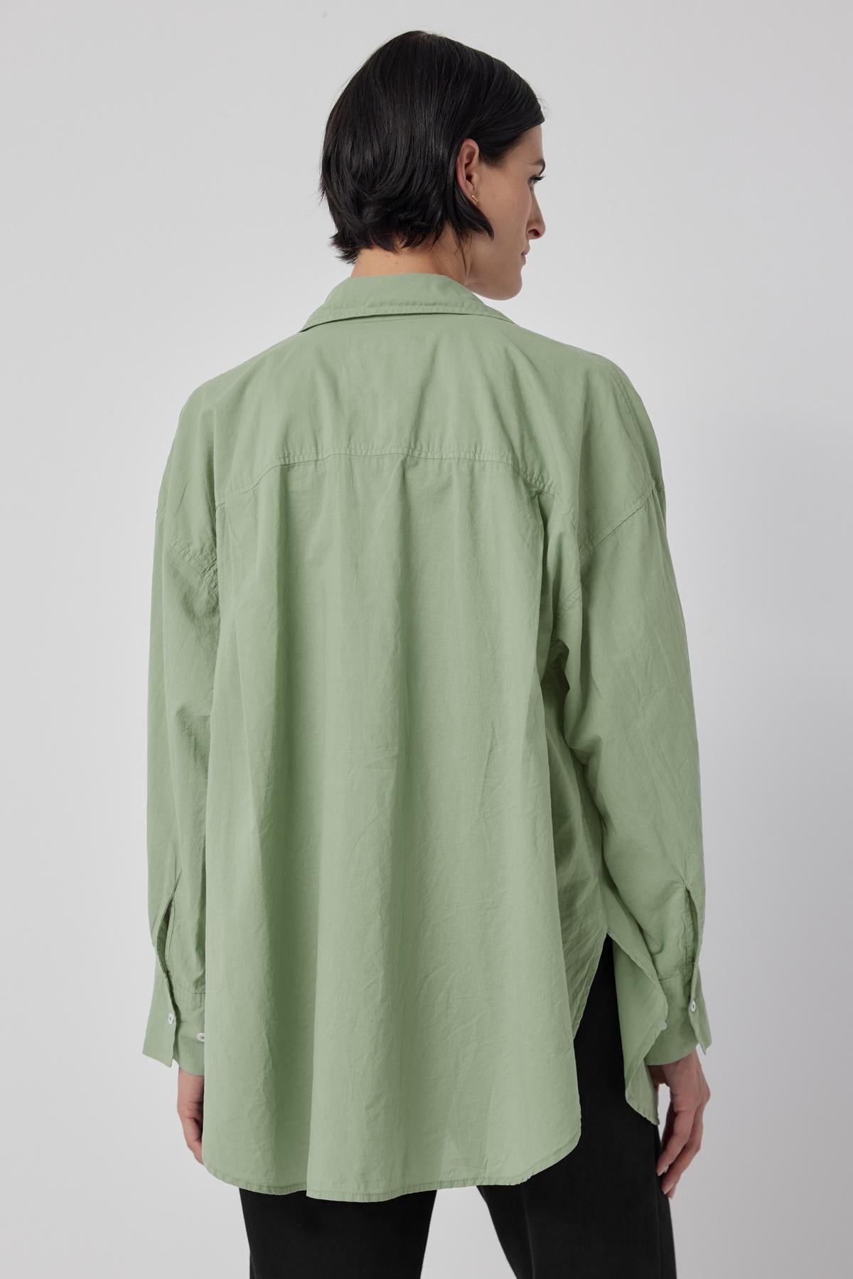 The back view of a woman wearing an oversized green cotton REDONDO BUTTON-UP SHIRT by Velvet by Jenny Graham with drop shoulder.-36198180094145