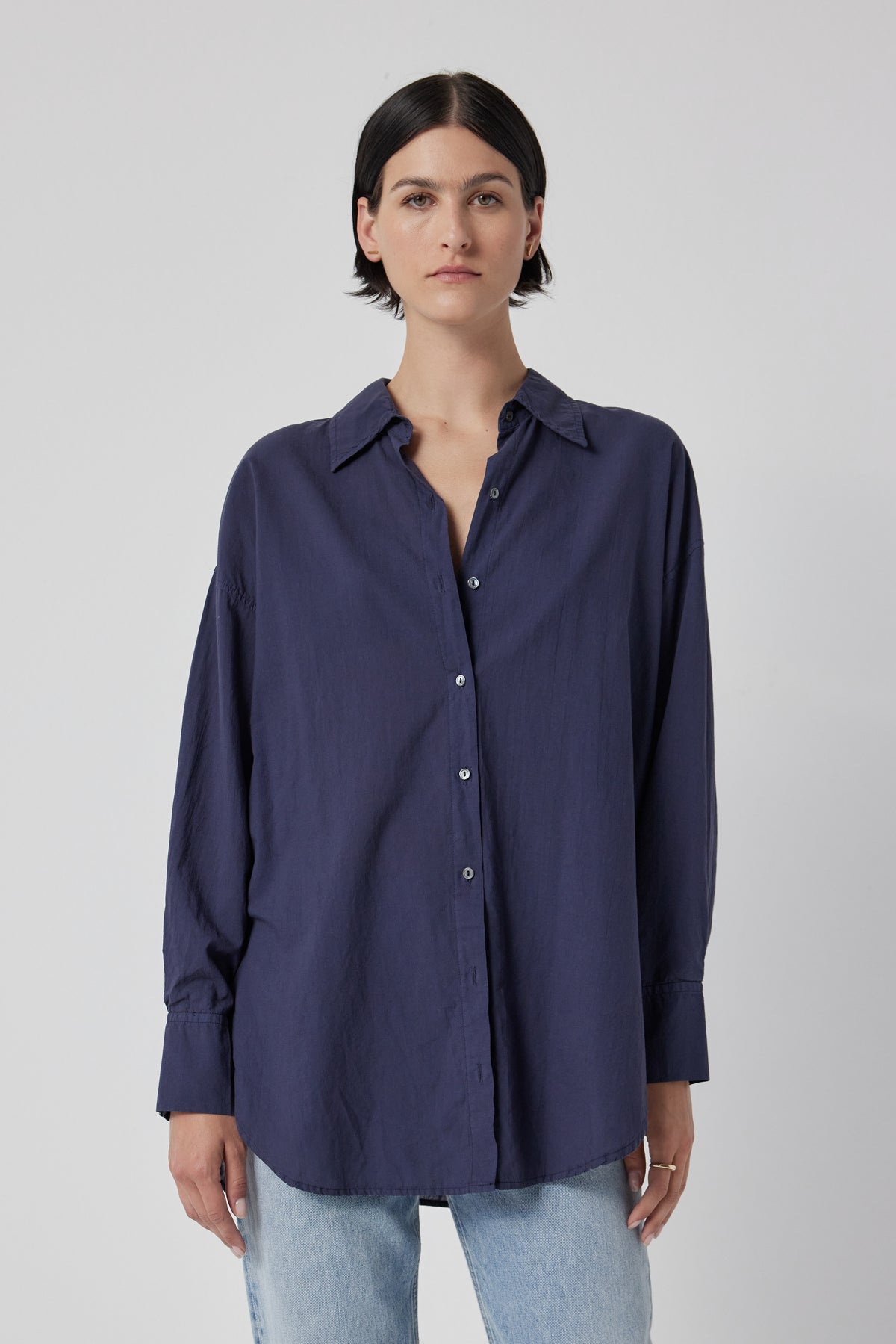 Woman wearing an oversized navy blue REDONDO BUTTON-UP SHIRT by Velvet by Jenny Graham and light blue jeans against a white background.-36168814624961