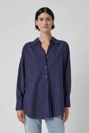Woman wearing an oversized navy blue REDONDO BUTTON-UP SHIRT by Velvet by Jenny Graham and light blue jeans against a white background.