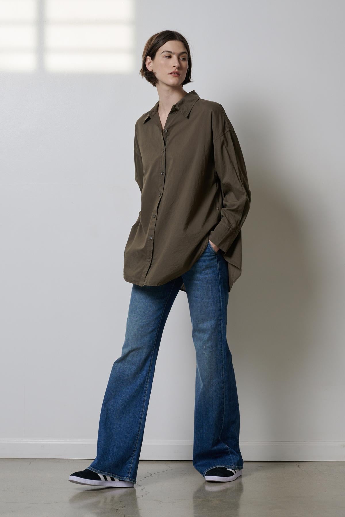   A woman is standing in a room wearing the REDONDO BUTTON-UP SHIRT by Velvet by Jenny Graham and oversized jeans. 