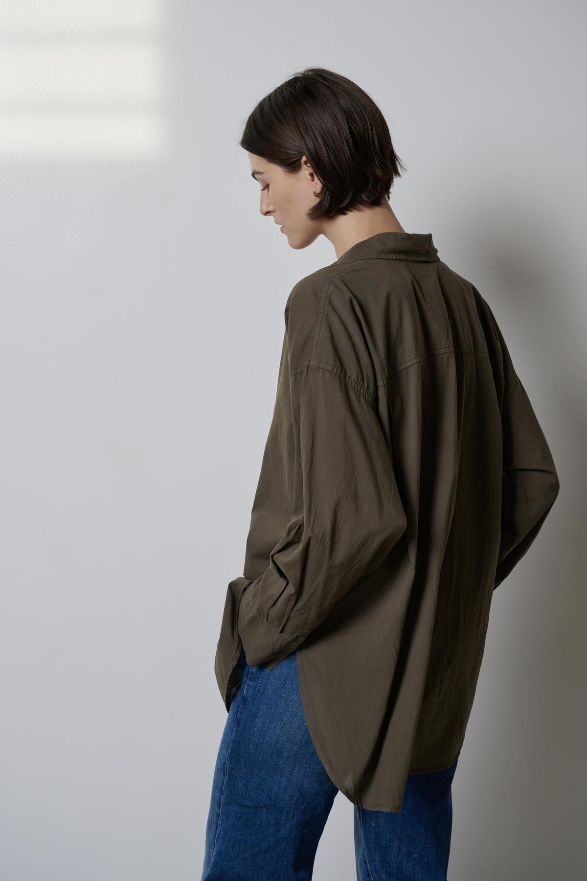 The borrowed-from-the-boys silhouette of a woman wearing jeans and an oversized Velvet by Jenny Graham REDONDO BUTTON-UP SHIRT showcases the soft cotton shirting.-35783065698497