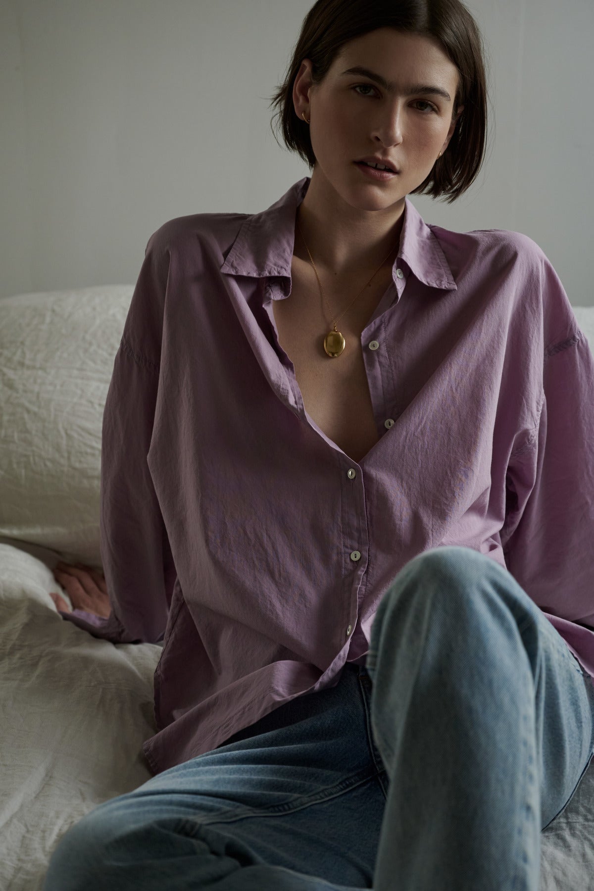 A woman in a Velvet by Jenny Graham REDONDO BUTTON-UP SHIRT and jeans sitting on a bed.-35783066190017