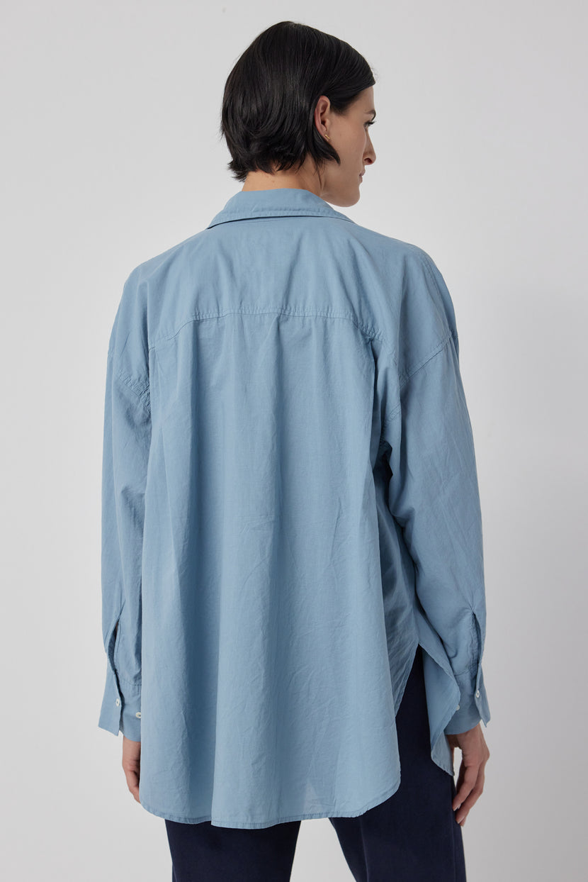 The back view of a woman wearing an oversized blue cotton Velvet by Jenny Graham REDONDO BUTTON-UP SHIRT.