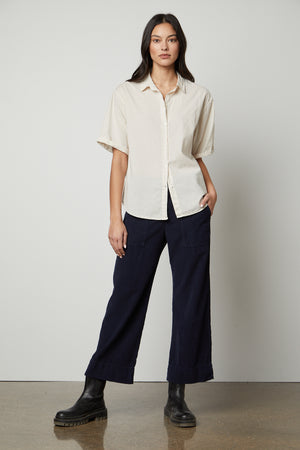 The model is wearing a Shannon Button-Up Shirt by Velvet by Graham & Spencer and navy trousers.