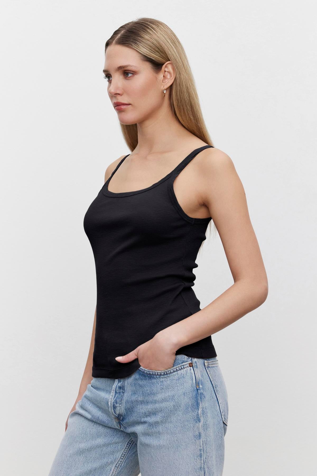 Woman in a black Aliza ribbed cotton layering tank top by Velvet by Graham & Spencer and blue jeans standing in profile against a white background.-36443834941633