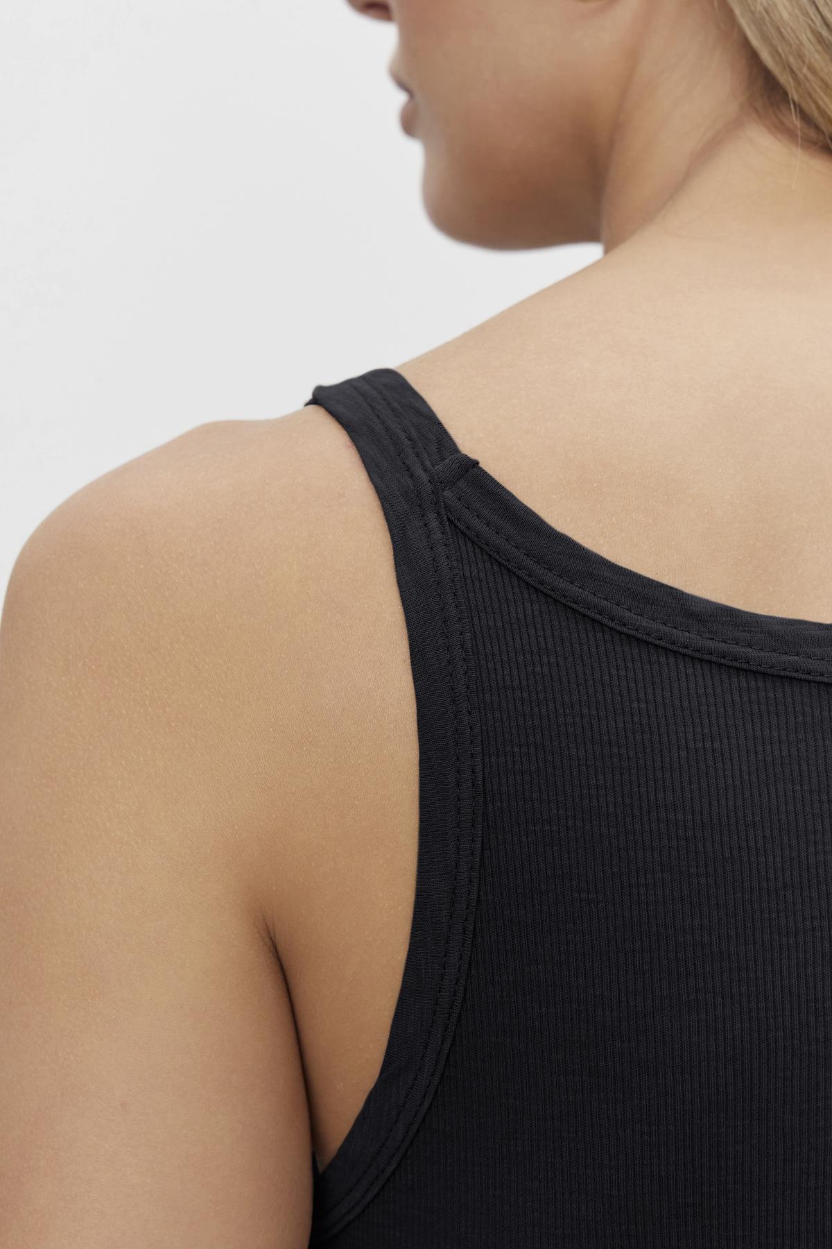 Close-up view of a person's shoulder wearing a black Aliza Ribbed Cotton Layering Tank by Velvet by Graham & Spencer.-36443835007169