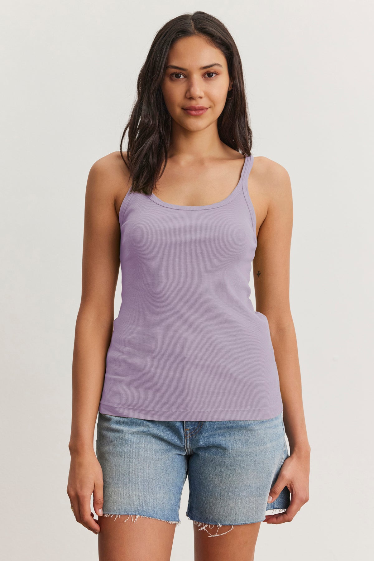 A person in Velvet by Graham & Spencer's ALIZA Ribbed Cotton Layering Tank and denim shorts poses against a plain backdrop, effortlessly showcasing the art of layering in their casual summer look.-38928230973633