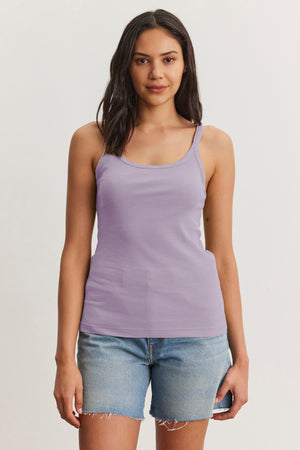 A person in Velvet by Graham & Spencer's ALIZA Ribbed Cotton Layering Tank and denim shorts poses against a plain backdrop, effortlessly showcasing the art of layering in their casual summer look.
